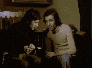 two men are sitting next to each other in a dark room and one is holding a cane