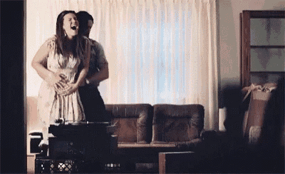 a man is holding a woman 's stomach in a living room while she laughs .