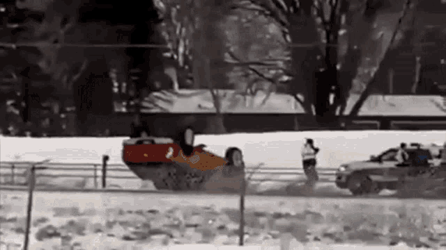 a red car is going down a snowy road .