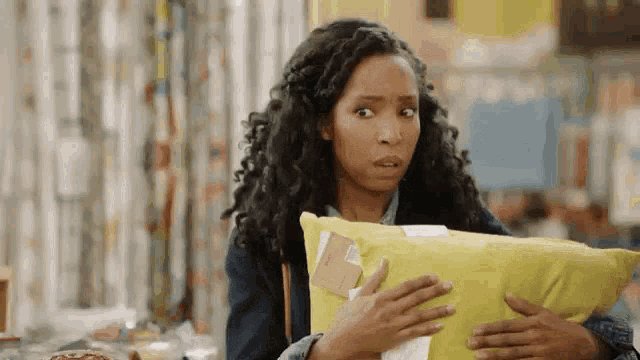 a woman is holding a yellow pillow and making a funny face .
