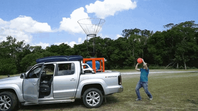 a man throws a frisbee in front of a silver pickup truck that says e motion