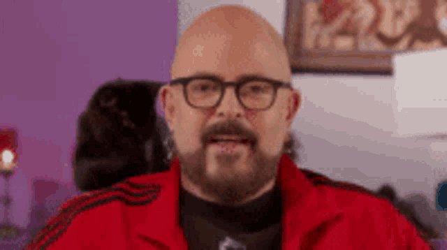 a bald man with a beard and glasses is wearing a red jacket and a black shirt .