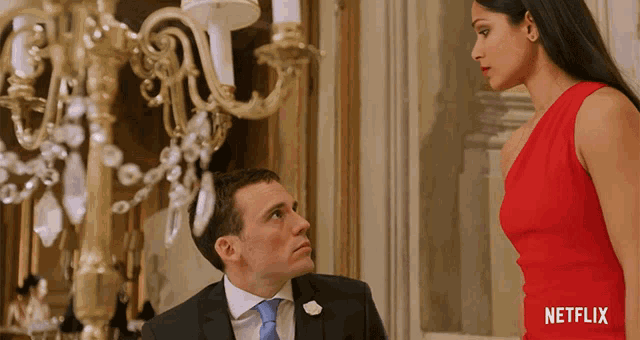 a man in a suit and tie is kneeling down next to a woman in a red dress with a netflix logo behind them