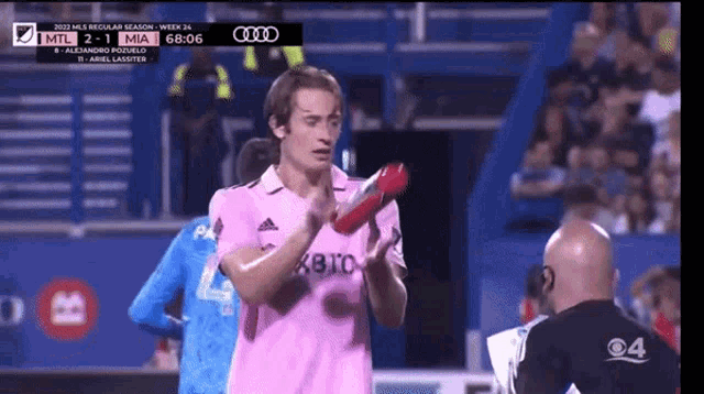 a soccer player wearing a pink jersey holds a red object in his hands