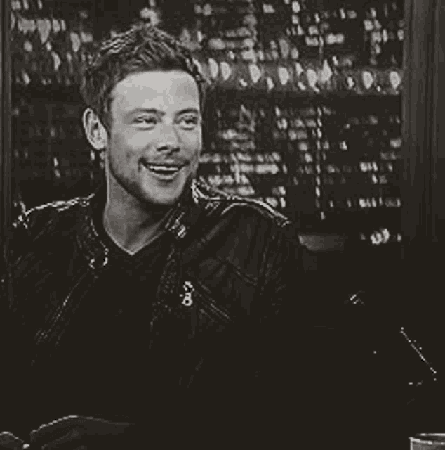 a black and white photo of a man in a leather jacket smiling