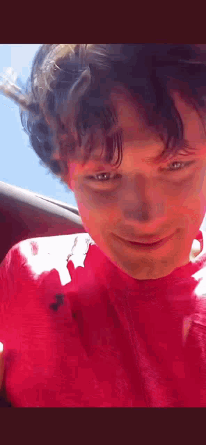 a young man wearing a red shirt is smiling and looking at the camera