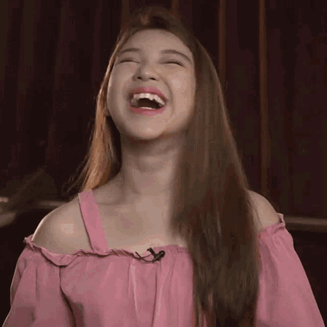 a woman in a pink off the shoulder top is laughing with her mouth wide open .