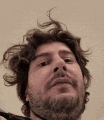 a man with a beard is looking at the camera with his hair blowing in the wind