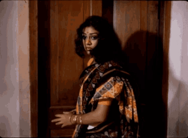 a woman in a black and yellow saree stands in front of a wooden door