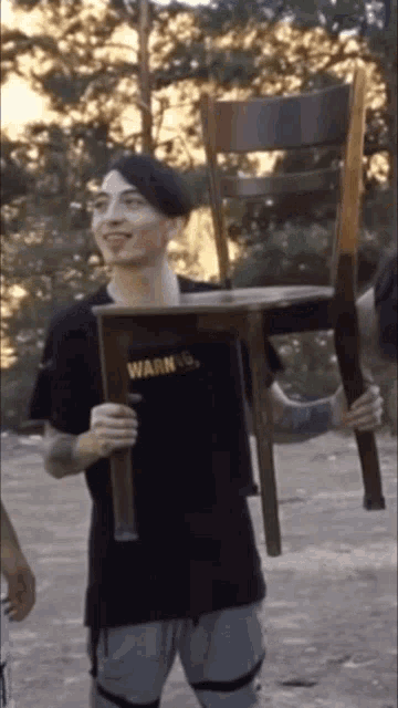 a man wearing a black shirt that says warning is holding a chair