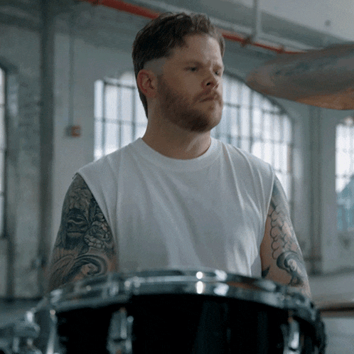 a man with a beard and tattoos is playing drums