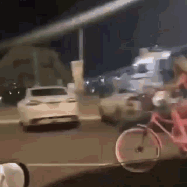 a car is driving down a street at night with a bicycle in the foreground .