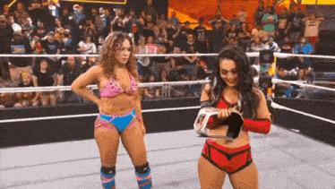 two women are standing in a wrestling ring and one is holding a trophy .