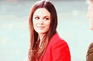 a woman in a red jacket is sitting next to a man and looking at the camera .