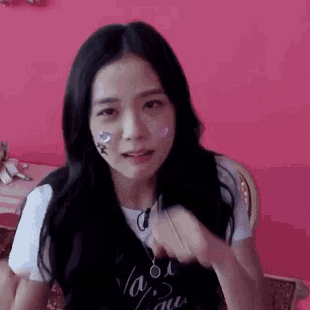 a girl with long black hair is sitting in front of a pink wall with stickers on her face .