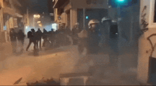 a group of people are walking down a street with a green light in the background