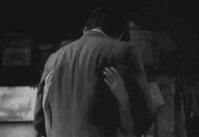 a black and white photo of a man and a woman hugging each other .