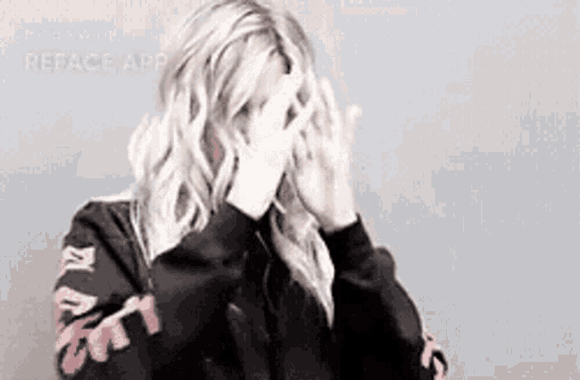 a woman is covering her face with her hands while wearing a black hoodie with a floral print on the sleeves .