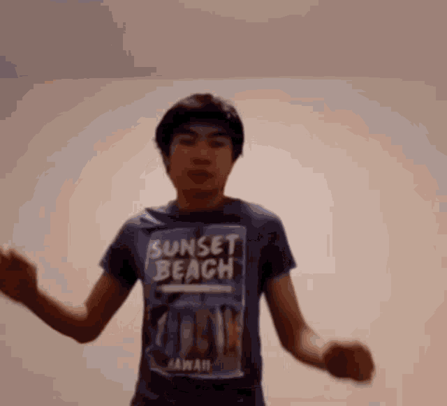 a young man wearing a sunset beach hawaii t-shirt is dancing in a room .