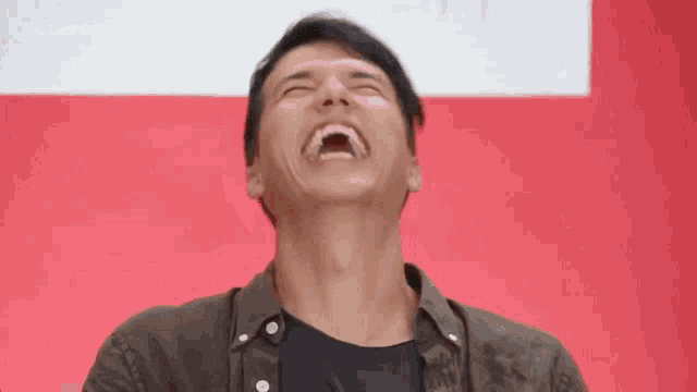 a man is laughing with his mouth open in front of a red wall .