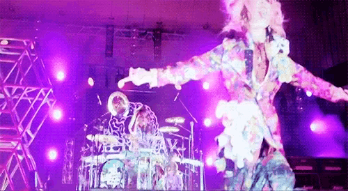 a man in a colorful suit is dancing on a stage with purple lights behind him .