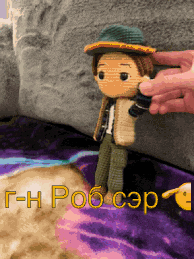 a person is holding a crocheted doll on a purple blanket that says t-h rob cep