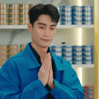 a man in a blue jacket is praying with his hands folded in front of a shelf filled with cans .