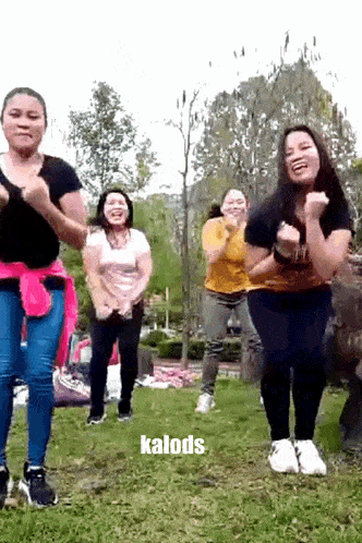 a group of women are dancing in a park with the word kalods on the bottom .