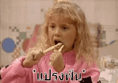 a little girl is brushing her teeth with a wooden toothbrush in a pink sweater .