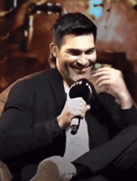 a man in a suit is holding a microphone in his hand and smiling .