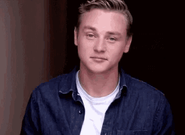 a young man wearing a blue shirt and a white t-shirt looks at the camera