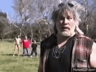 a man in a plaid vest is standing in a field with a group of people standing behind him .
