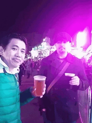 a man in a green jacket holds a cup of beer next to another man