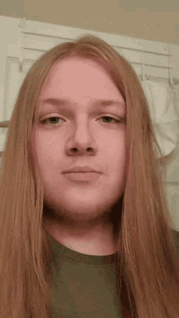 a young man with long red hair and green eyes looks at the camera .