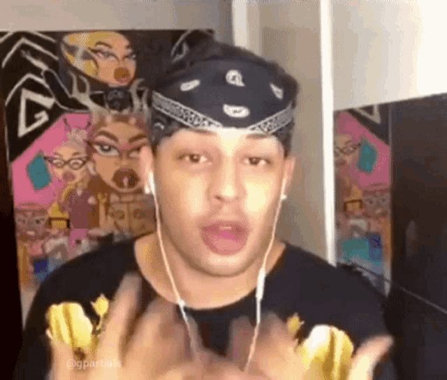 a man wearing a bandana and headphones is making a funny face in front of a painting .