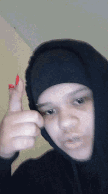 a woman wearing a black hoodie is giving a thumbs up sign