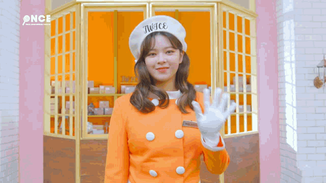 a woman wearing an orange jacket and a white hat with the word twice on it .