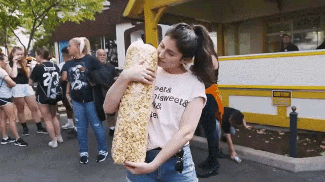 a woman holding a large bag of popcorn wearing a t-shirt that says beets nisweets