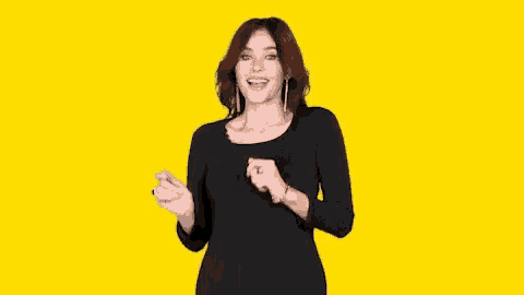 a woman in a black dress is dancing and smiling on a yellow background