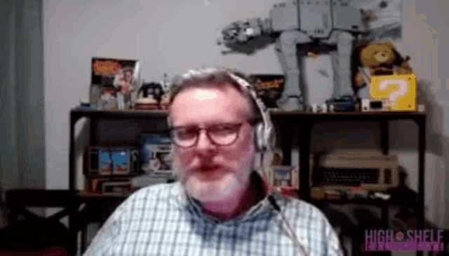 a man wearing headphones is sitting in front of a shelf with toys on it and a sign that says high shelf