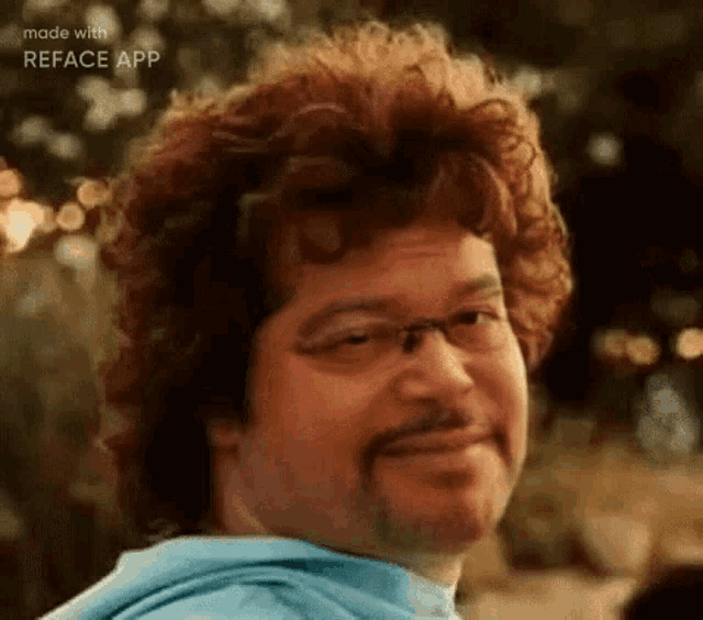 a man with curly hair and glasses is smiling and wearing a blue hoodie .