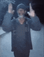 a man with a beard wearing a hat and a jacket is making a peace sign .