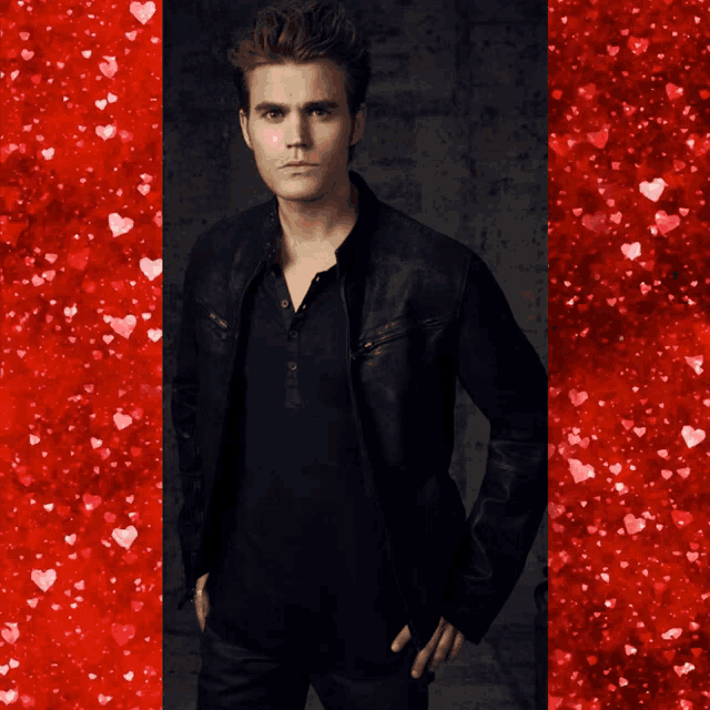 a man with his hands in his pockets is standing in front of a red background with hearts