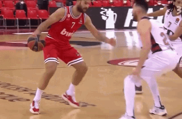 a basketball player in a red jersey is dribbling the ball while another player in a white jersey tries to block him .