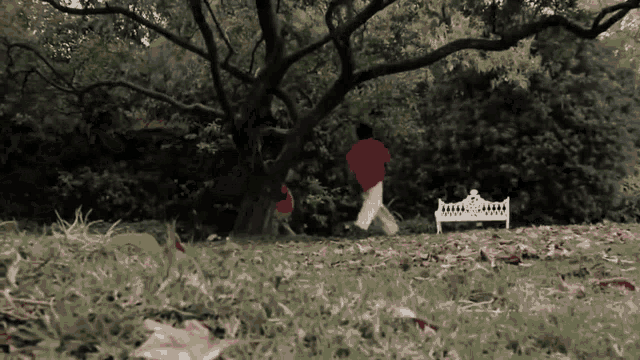 a person in a red shirt is running in a park near a white bench