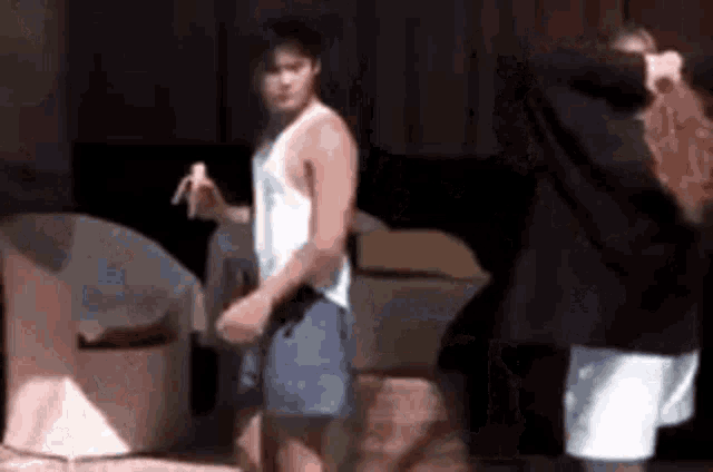 a man in a white tank top is holding a banana while a woman stands behind him .