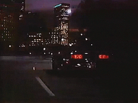 a car is driving down a road at night with a city in the background .