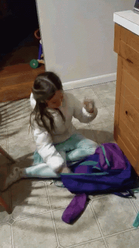 a little girl is sitting on the floor with a backpack