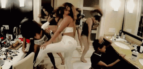 a group of women are dancing in a bathroom while another woman blow drying their hair .