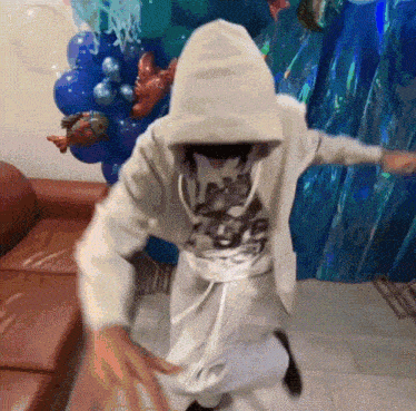 a person in a hoodie is dancing in front of balloons and a couch
